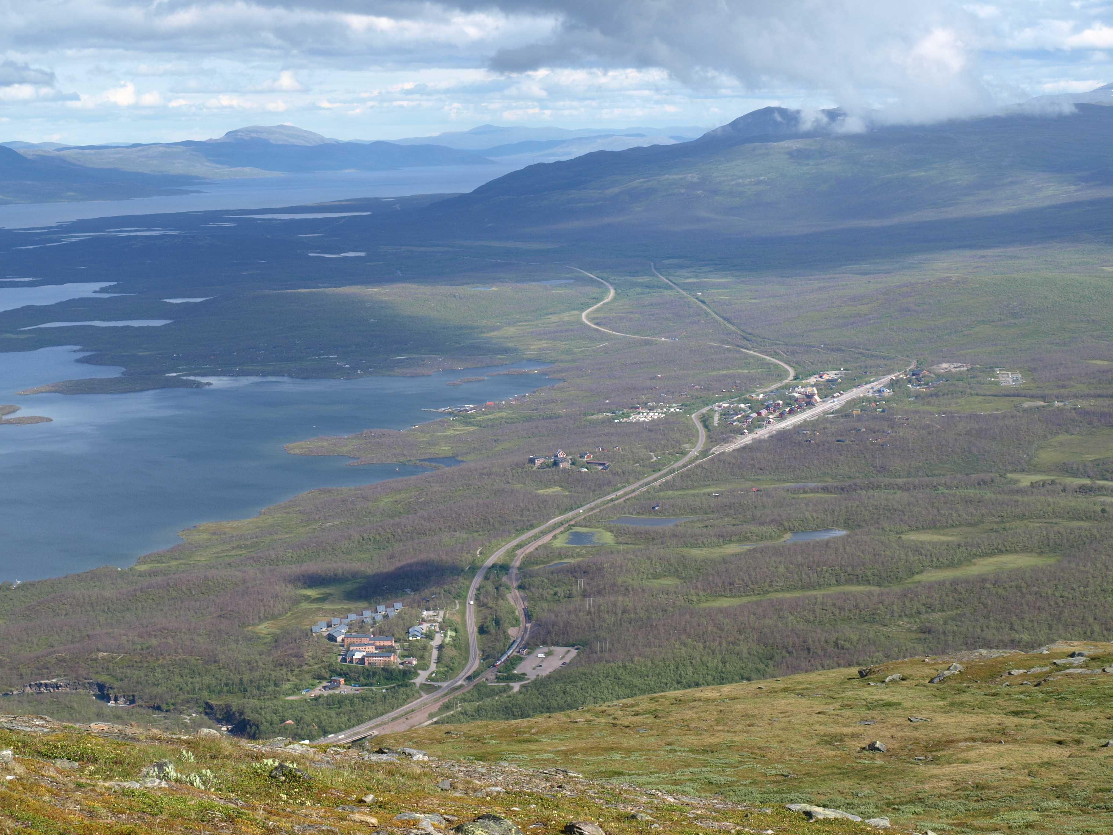 Overview of Abisko in the background, showing a vast landscape from above with forests in the foreground and mountains in the background